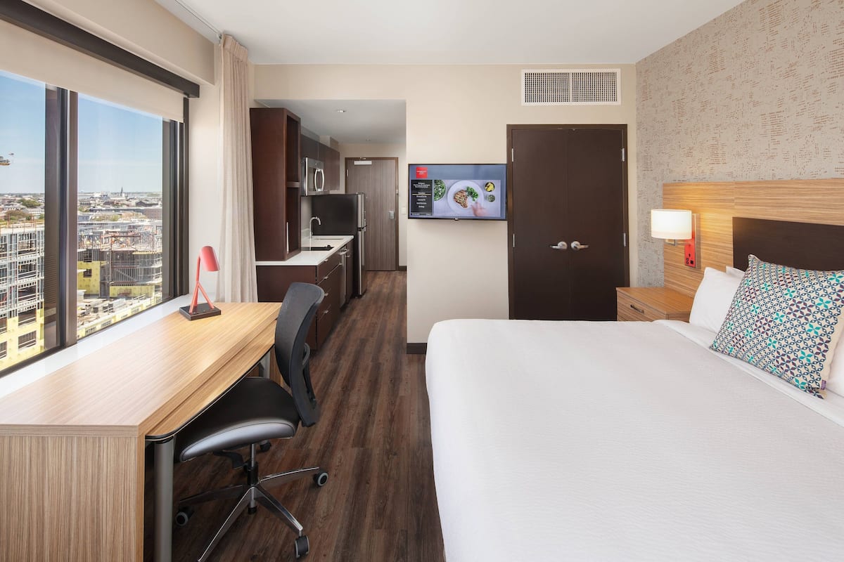 A hotel room with a large bed, a desk with a chair, a TV, and a view of the city.