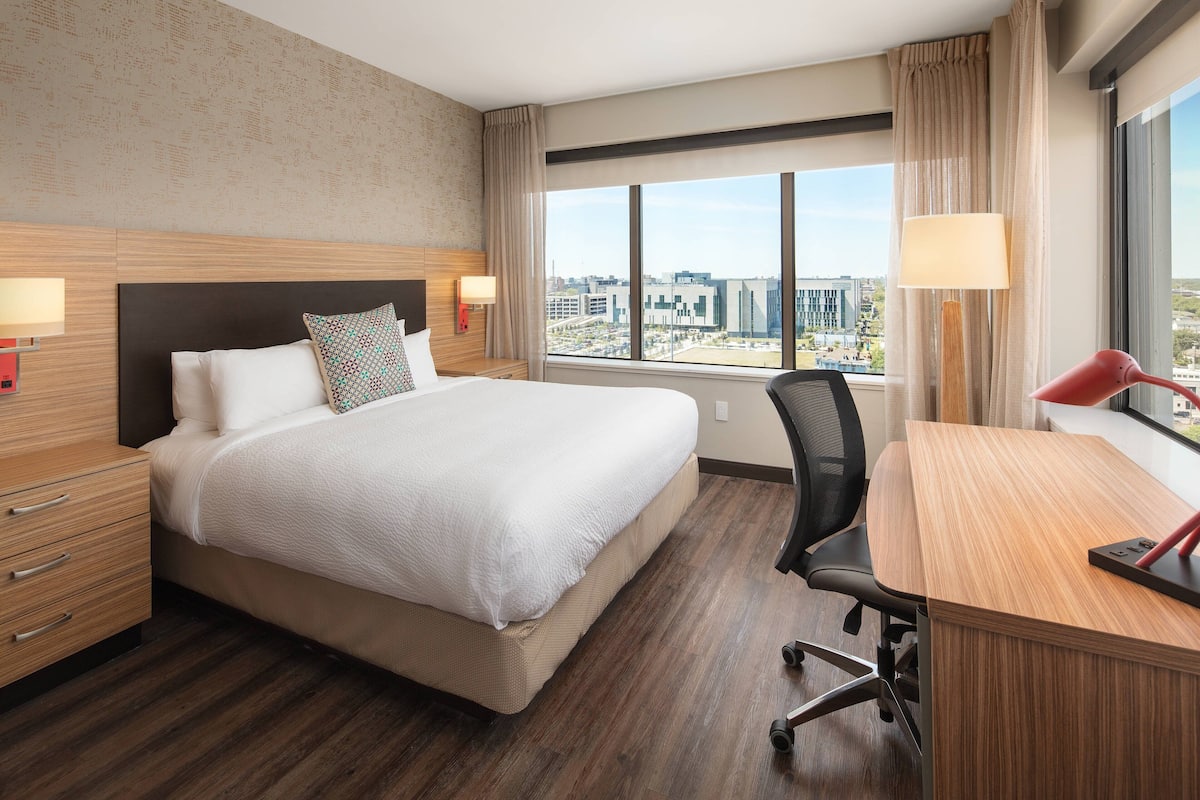 A hotel room with a large bed, a desk, and a view of the city.