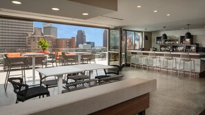 A modern bar area with a city view, featuring a bar counter, seating, and a large window overlooking the cityscape. - TownePlace Suites New Orleans Downtown/Canal Street (New Orleans)