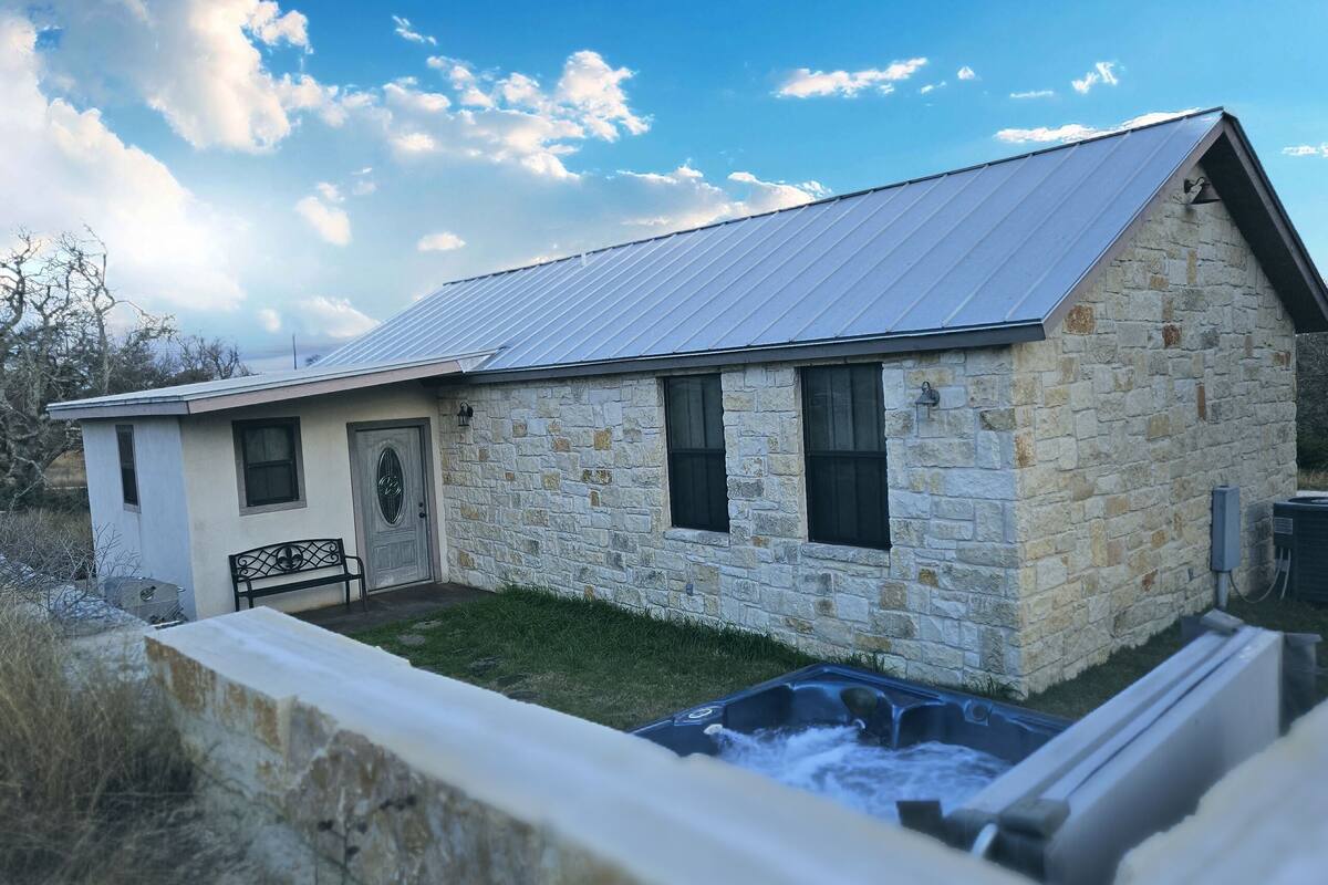A stone building with a metal roof, a front door, and a small patio area.