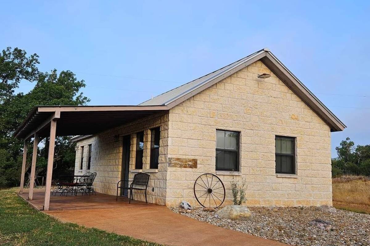 A stone building with a covered porch, a large wheel, and a sign.