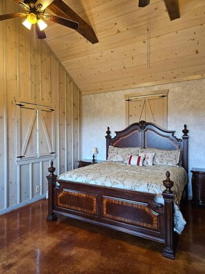A bedroom with a wooden ceiling, a large bed with ornate headboard, and a ceiling fan.