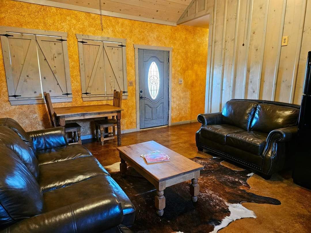 Ein Zimmer mit Holzboden, einem schwarzen Ledersofa, einem Holztisch und einem Kuhfellteppich.