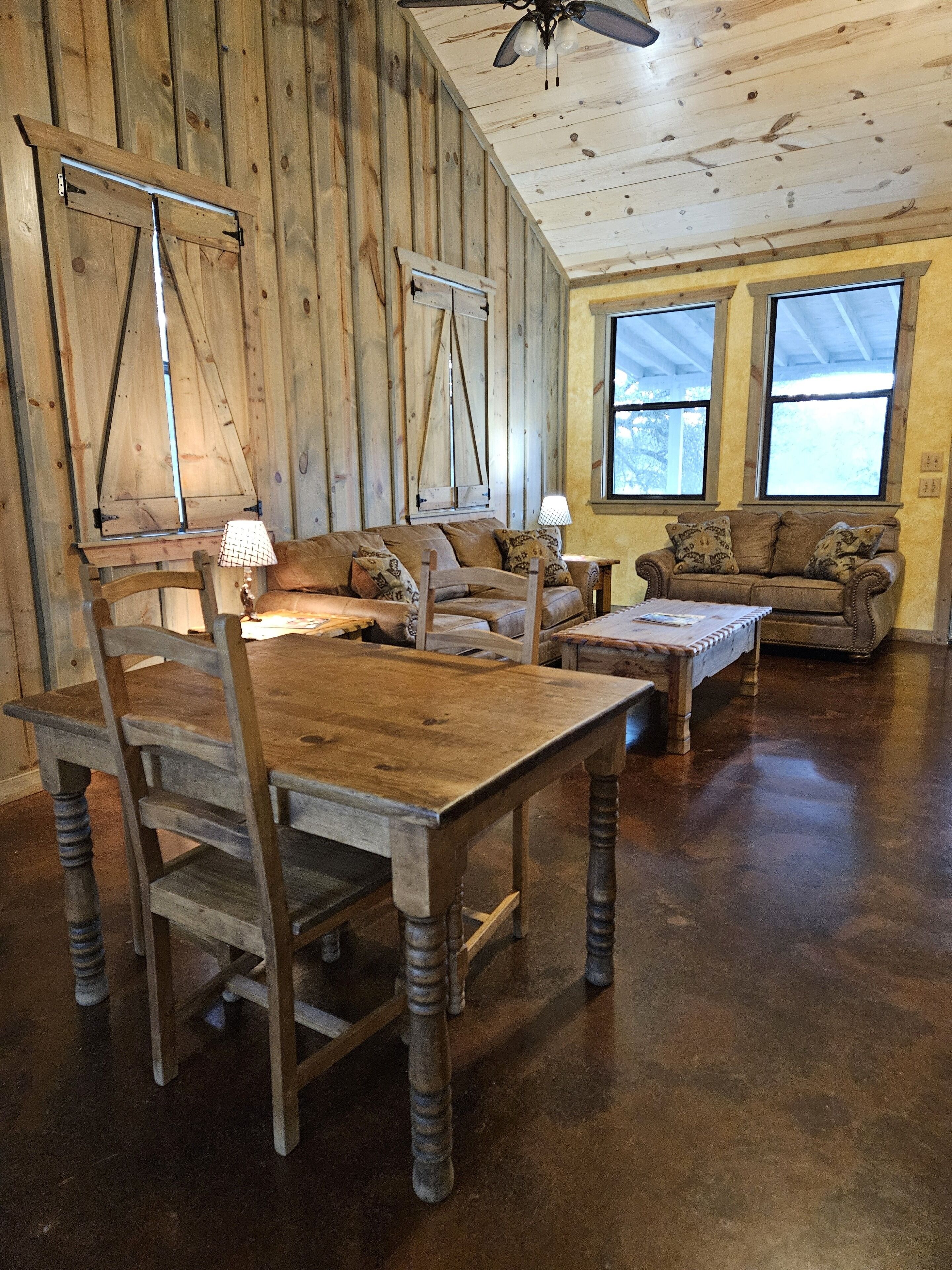 A rustic wooden interior with a dining table, chairs, a sofa, and a ceiling fan.