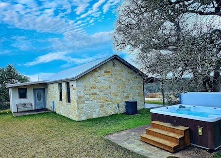 A stone house with a small porch and a hot tub in the backyard.