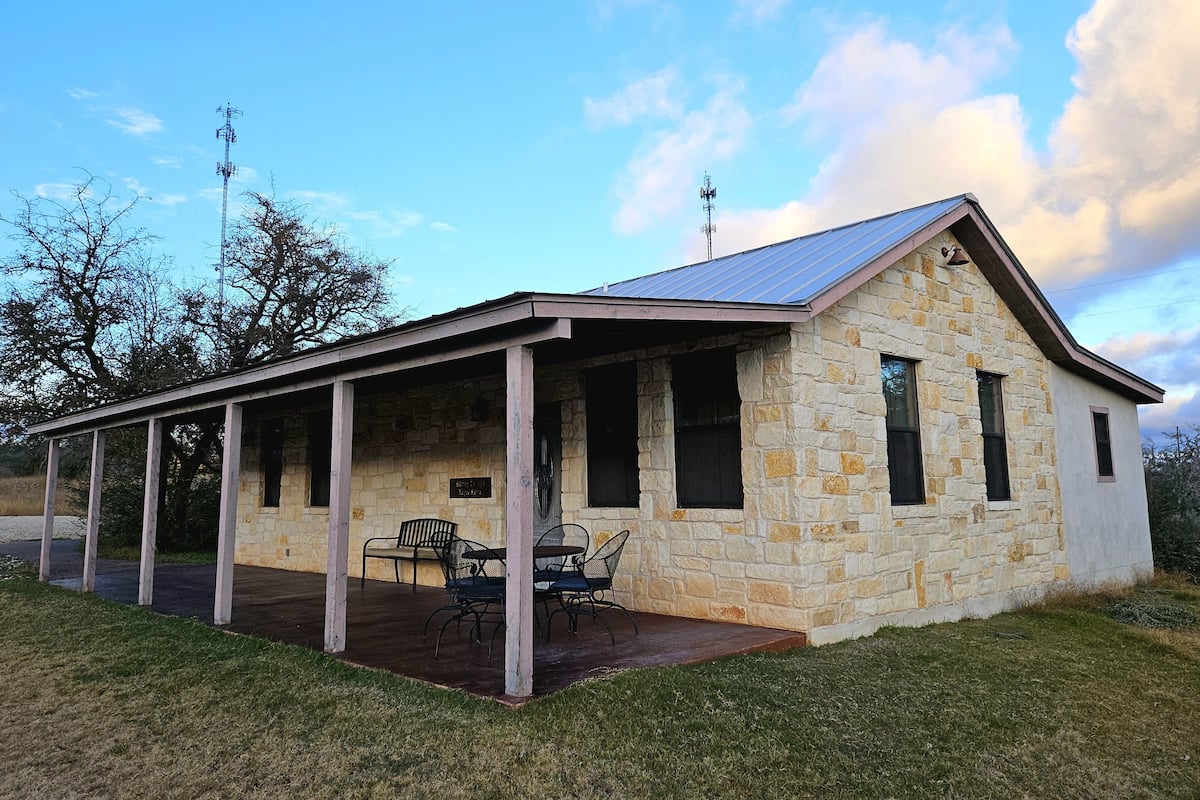 A small stone building with a covered porch, a stone chimney, and a metal roof.