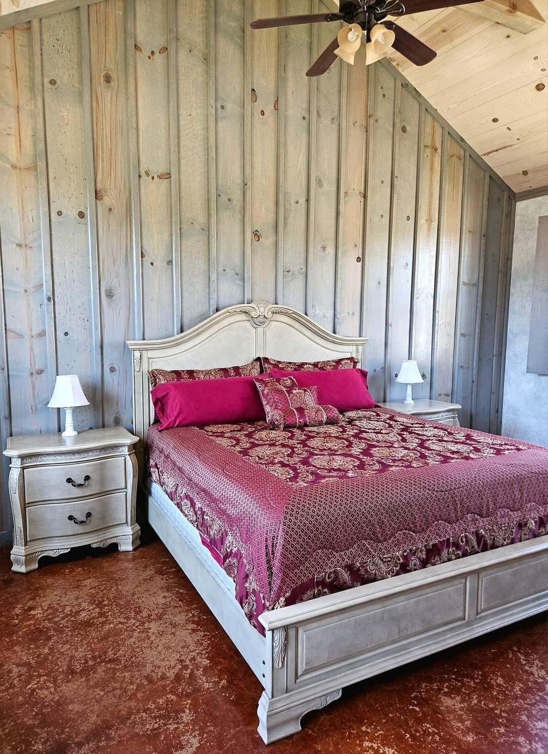 Una camera da letto con soffitto in legno, un letto con poggiatesta bianco, due comodini con lampade e una coperta a letto con motivo rosso.