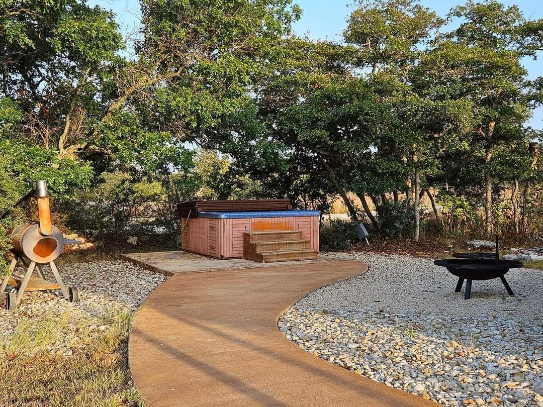 A hot tub in a garden with a gravel path and a fire pit.