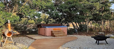 Un jacuzzi en un jardín con un camino de grava y una fogata.