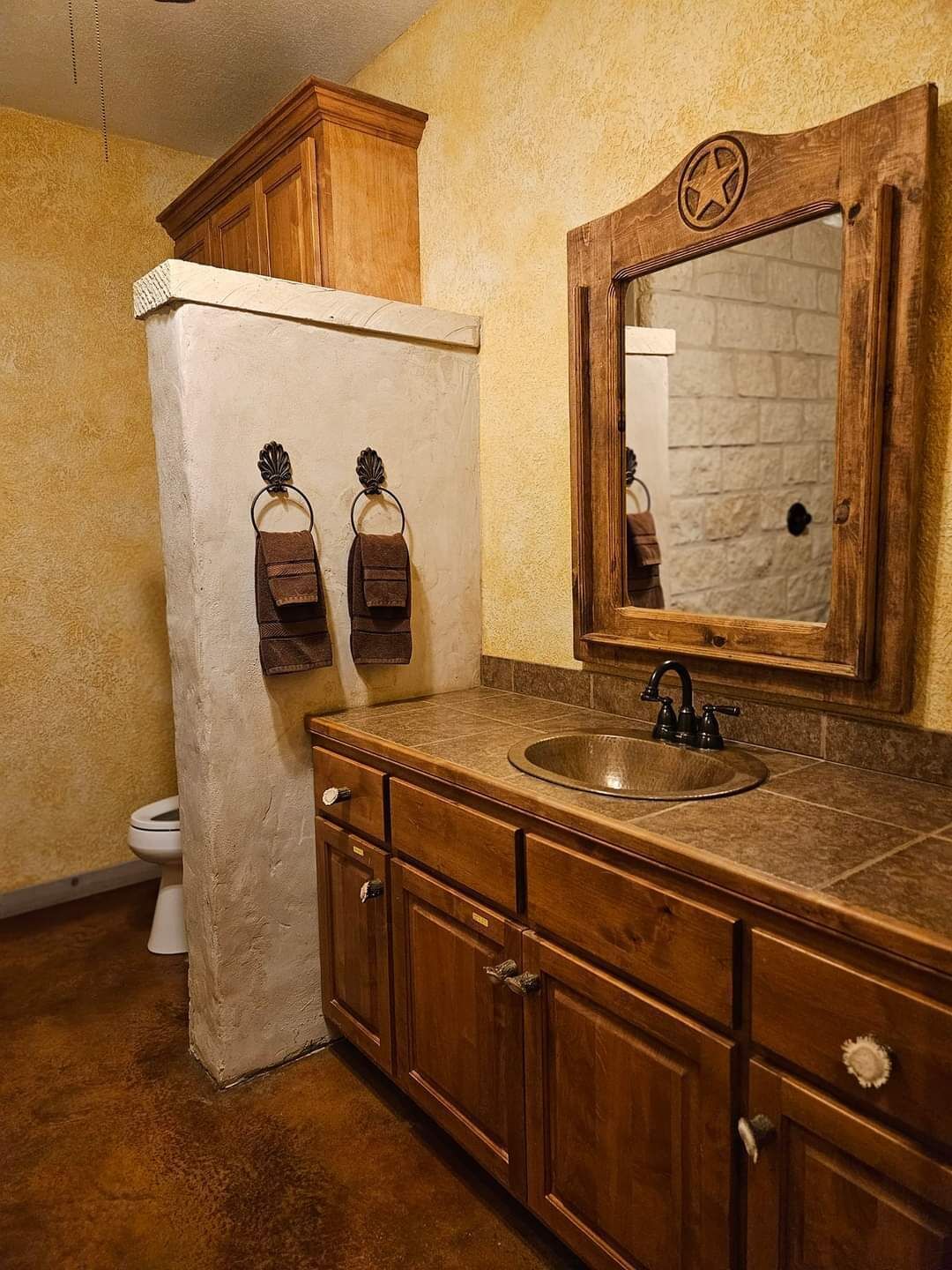A bathroom with a wooden vanity, a sink, a mirror, and a toilet.