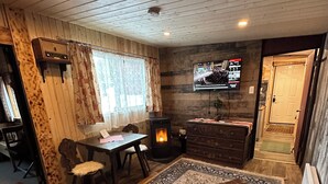 A cozy living room with a fireplace, a television mounted on the wall, a dining area with a table and chairs, and a sofa. - Guest House Austria (Stewart)