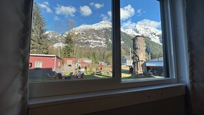 A window view of a mountainous landscape with a red building and a tree stump. - Guest House Austria (Stewart)