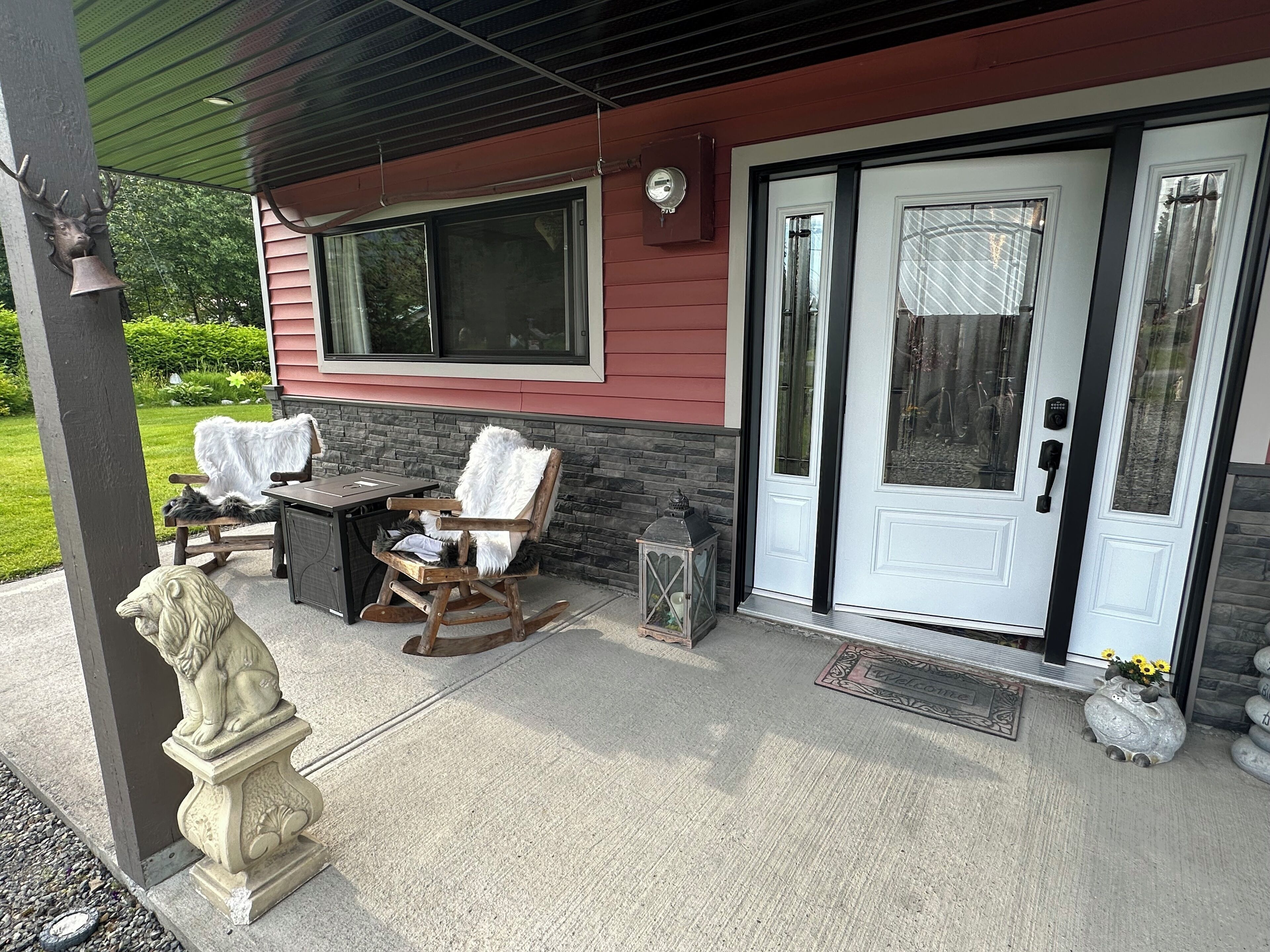 A covered porch with a table and chairs, a statue, and a welcome mat.
