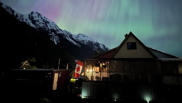 A building with a Canadian flag, snow-covered mountains, and the aurora borealis in the background. - Guest House Austria (Stewart)