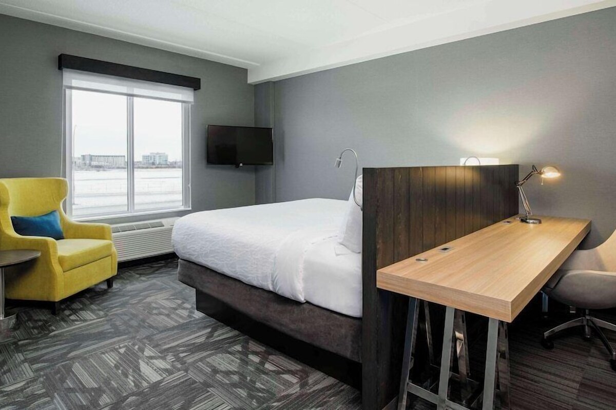 A hotel room with a bed, a desk, a chair, a TV, and a window with a view.