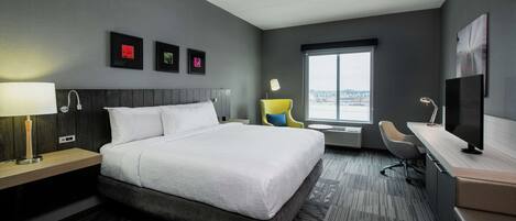 Habitación de hotel moderna con una cama grande, un escritorio, una silla y una ventana con vistas a la ciudad.