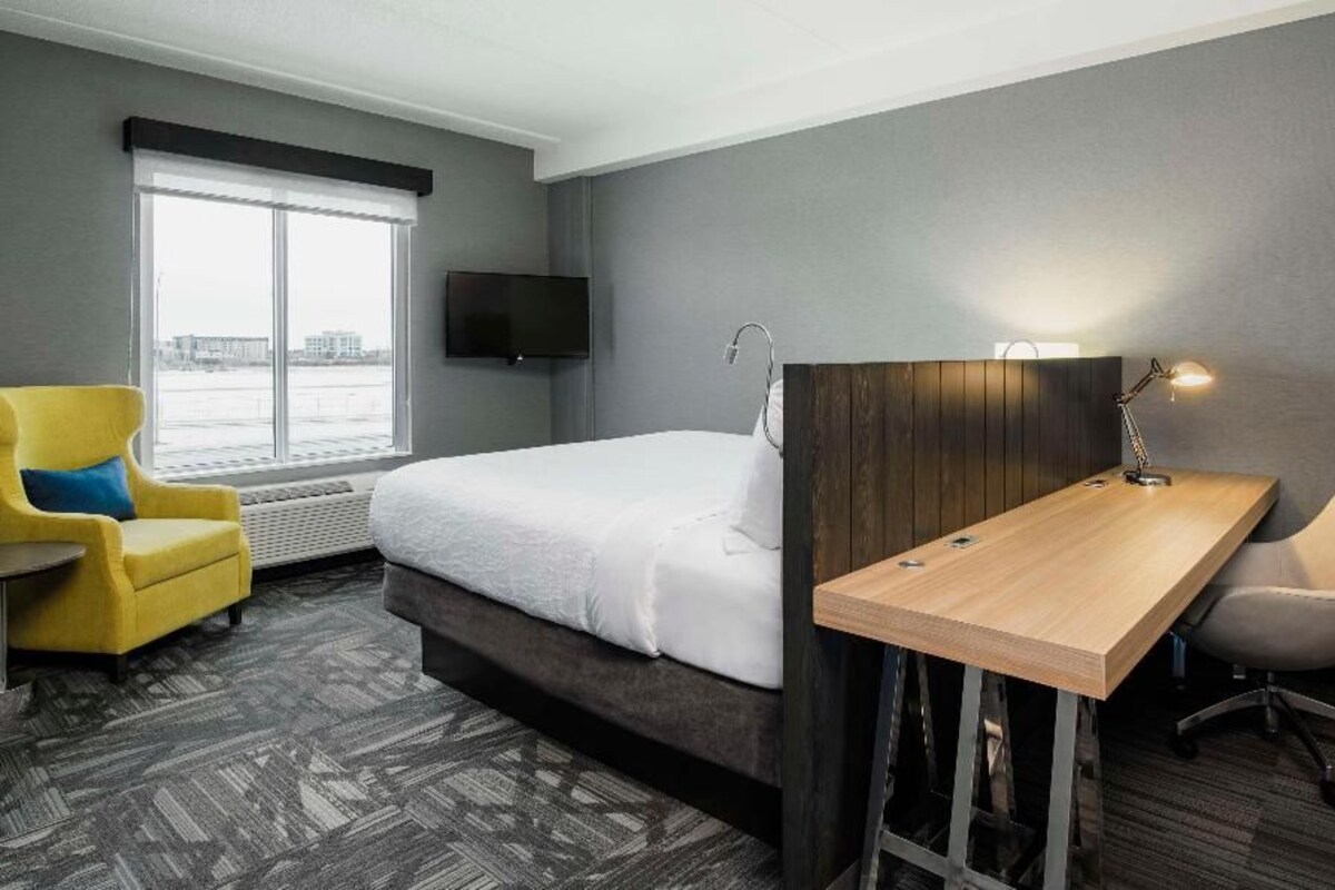 Une chambre d’hôtel équipée d’un lit, d’un bureau, d’une chaise, d’une télévision et d’une fenêtre donnant sur un paysage agréable.
