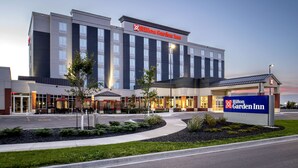 Un hotel Hilton Garden Inn con una facciata moderna, diversi ingressi e un'area verde piantumata sul davanti.