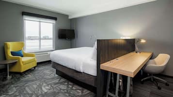 A hotel room with a bed, a desk, a chair, a TV, and a window with a view of buildings.