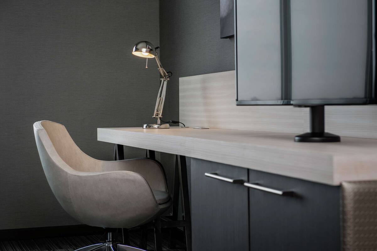 A modern office chair, a desk with a lamp, and a television mounted on a cabinet.