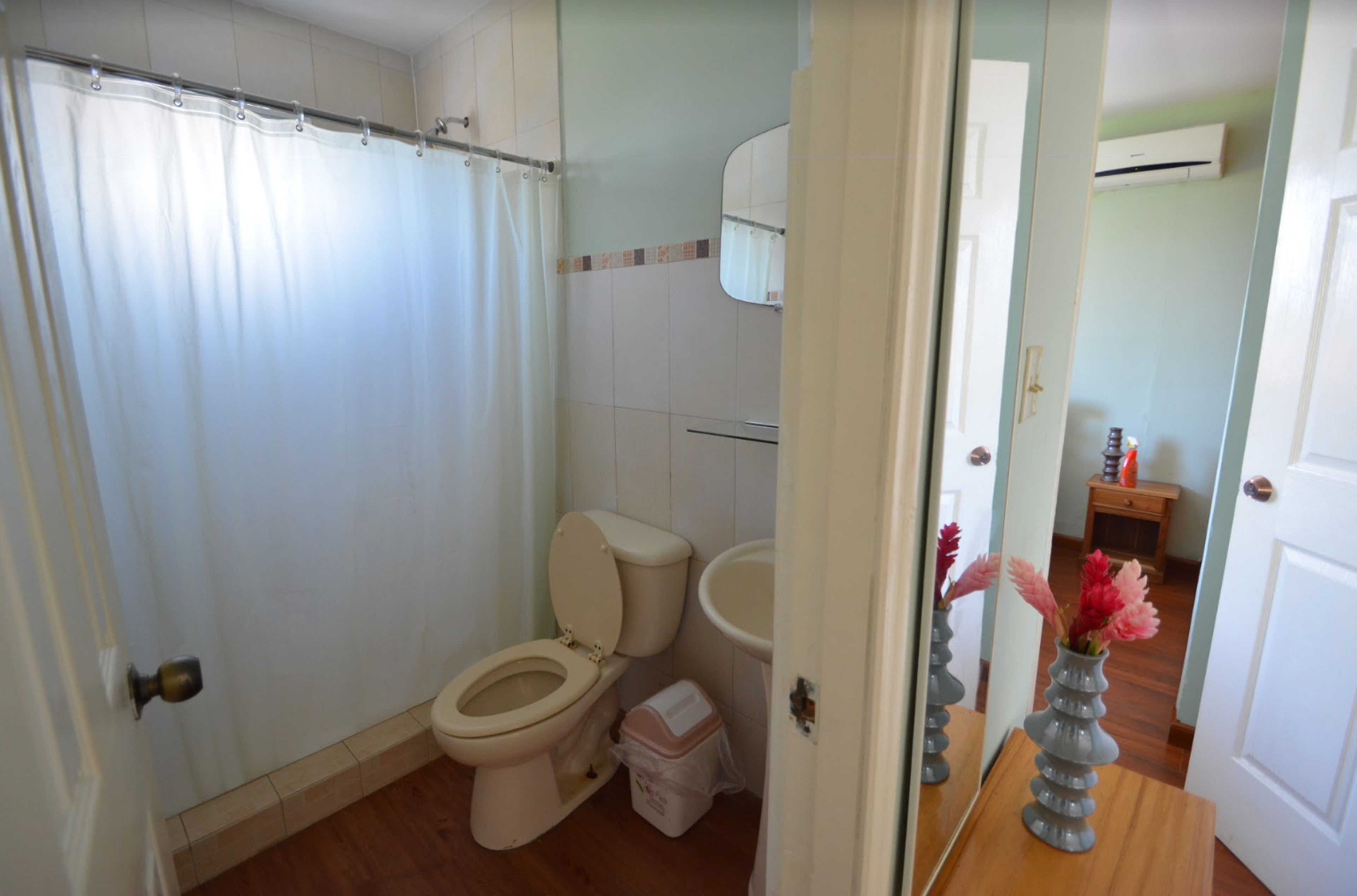 Een badkamer met een douche, toilet, wastafel en een spiegel die een vaas met bloemen weerspiegelt.