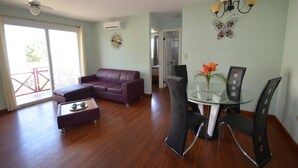 A spacious living area with a purple sofa, a glass dining table with chairs, and a ceiling fan. - Caribbean Villages Apartments (Bocas del Toro)
