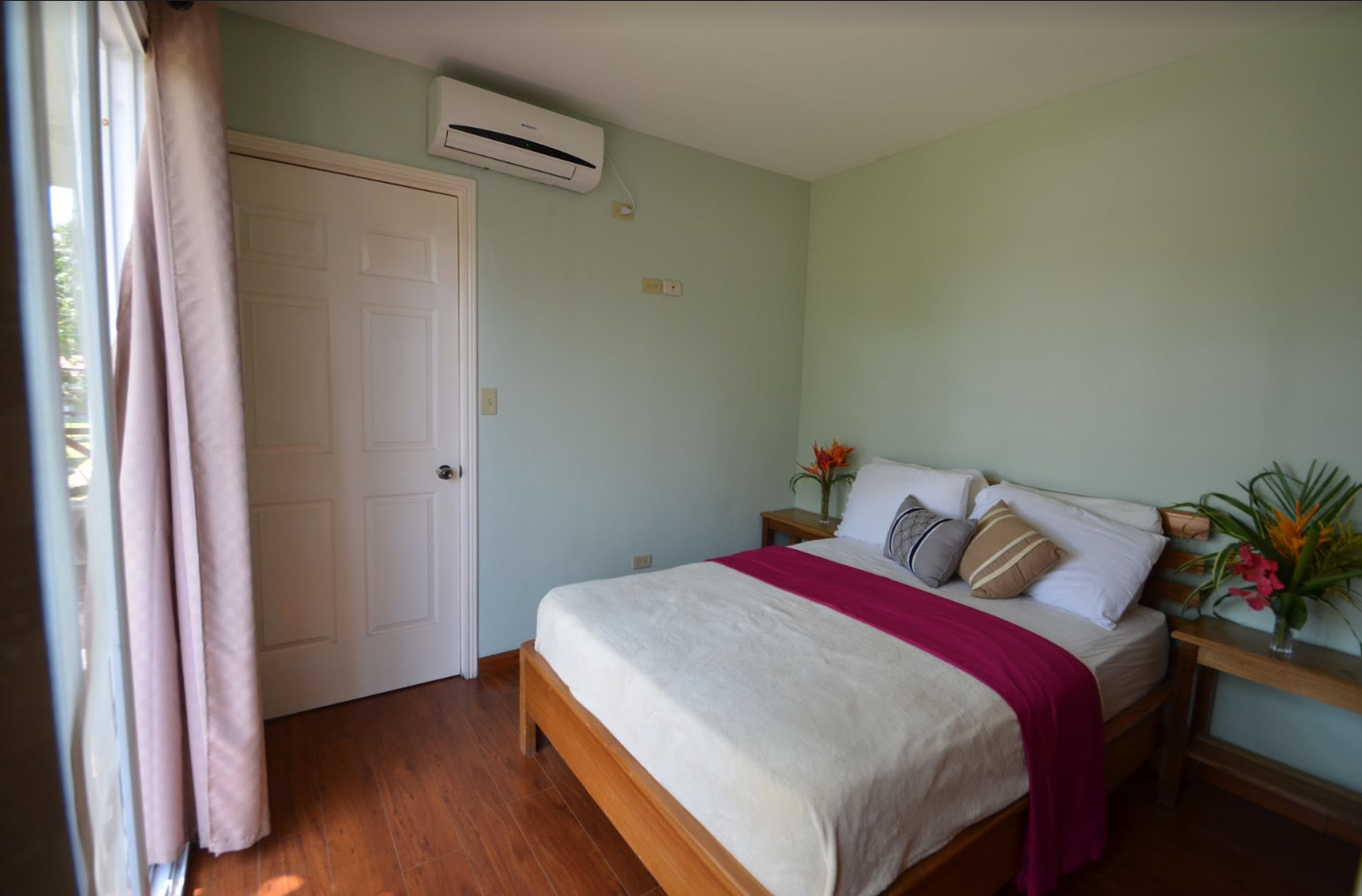 Une chambre à coucher avec un lit, une table de chevet, une fenêtre avec des rideaux et un climatiseur fixé au mur.
