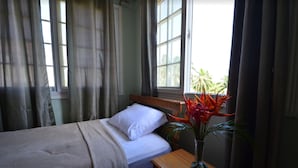 A neatly made bed with white bedding, a wooden nightstand with a vase of flowers, and a window with curtains. - Caribbean Villages Apartments (Bocas del Toro)