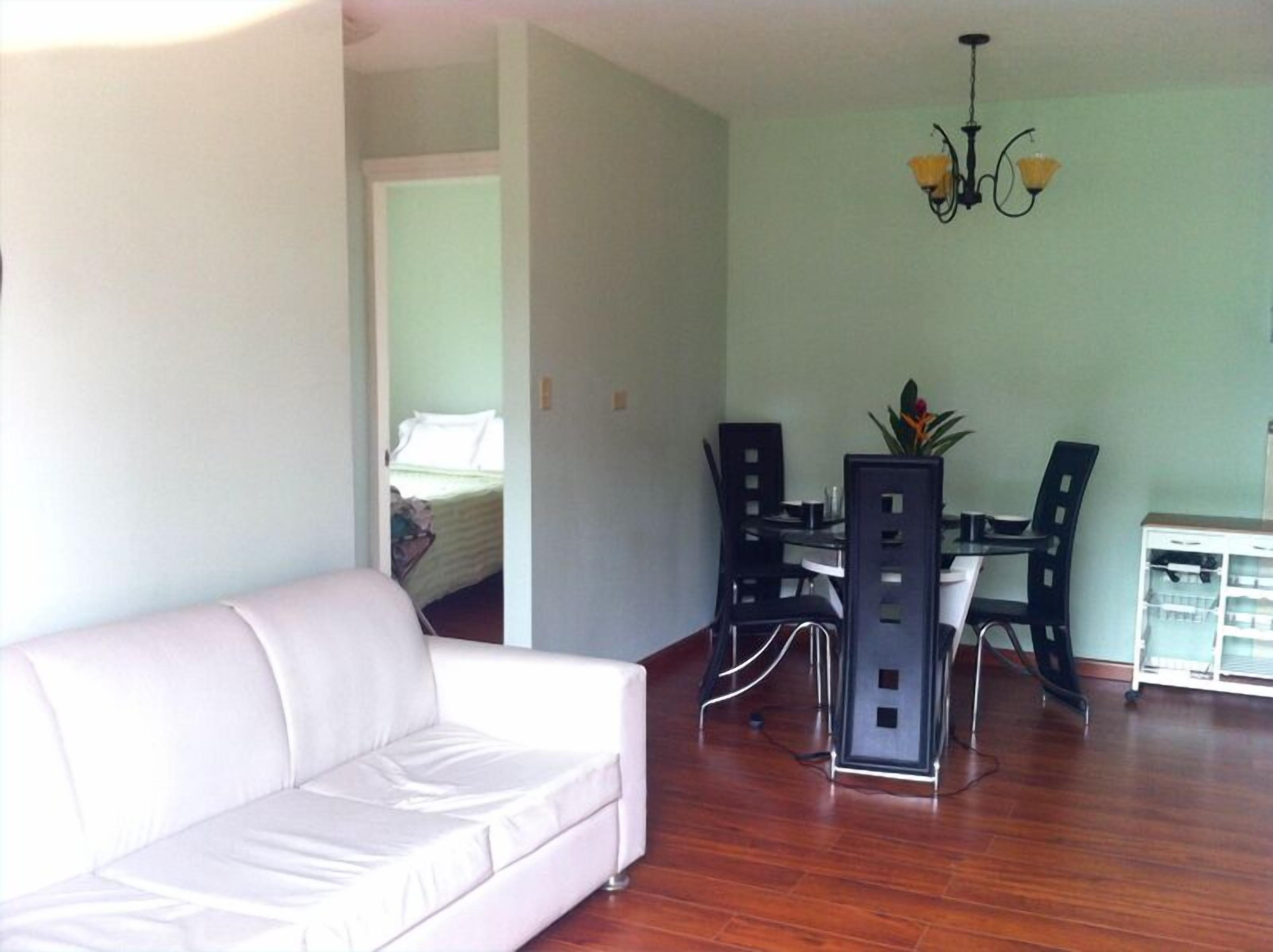 A living room with a white sofa, a dining table with chairs, and a chandelier.