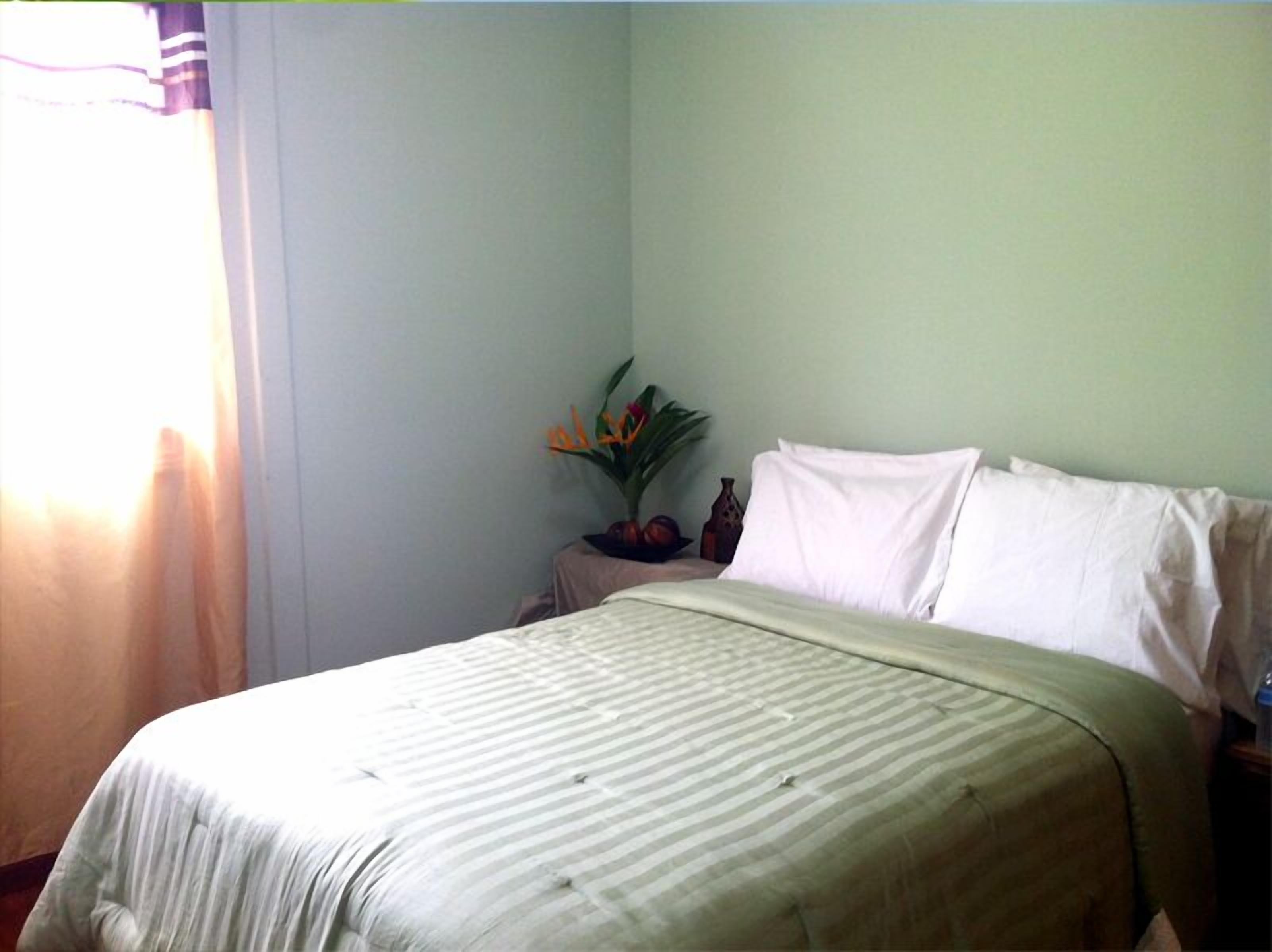 A neatly made bed with a striped bedspread, a bedside table with a vase of flowers, and a window with curtains.