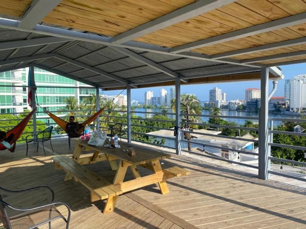 Eine Terrasse im Freien mit einem Holztisch und Stühlen, einer Hängematte und Blick auf eine Stadtlandschaft über dem Wasser.