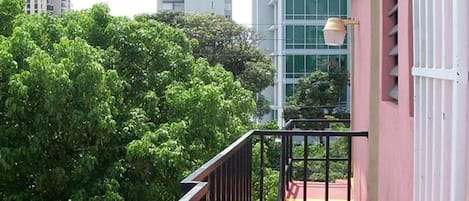 A balcony with a red floor, metal railing, and a view of tall buildings and dense greenery.