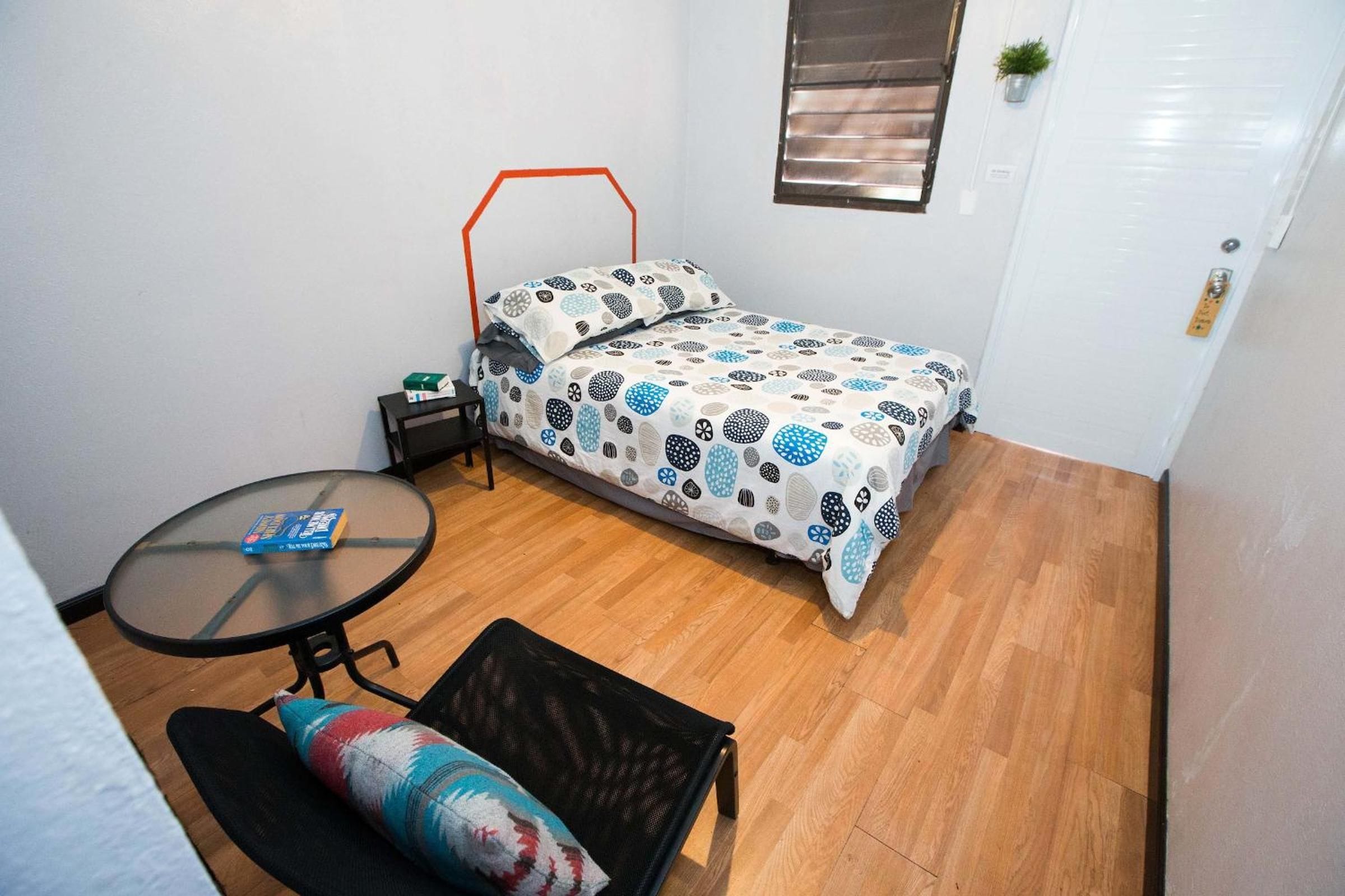 A compact room with a bed, a small table, a bench, and a window.