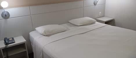 Una cama bien hecha con sábanas blancas, dos mesitas de noche y una lámpara de pared.