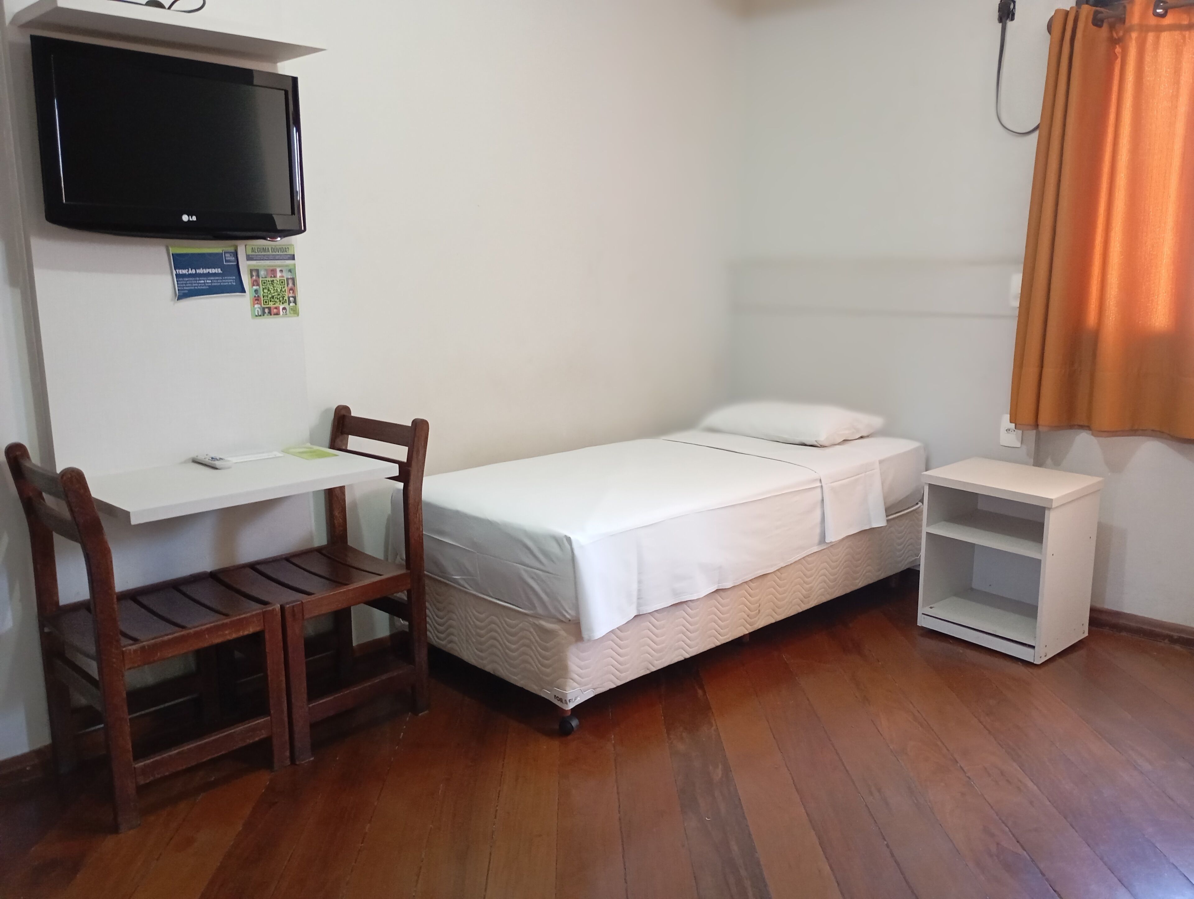 A small, neatly arranged room with a bed, a desk, and a chair.