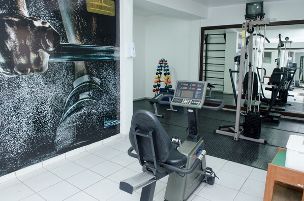 Ett gym med träningsutrustning, ett löpband och en vägg med en stor affisch.
