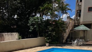 Una piscina rectangular con borde de azulejos, rodeada por un patio con mobiliario exterior.
