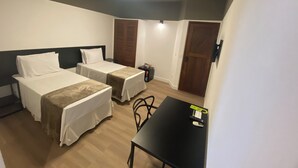 Una habitación de hotel compacta con dos camas individuales, una mesita y un escritorio.