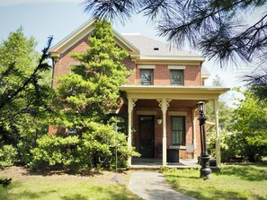 A two-story brick house with a porch, a front door, and a small garden area.