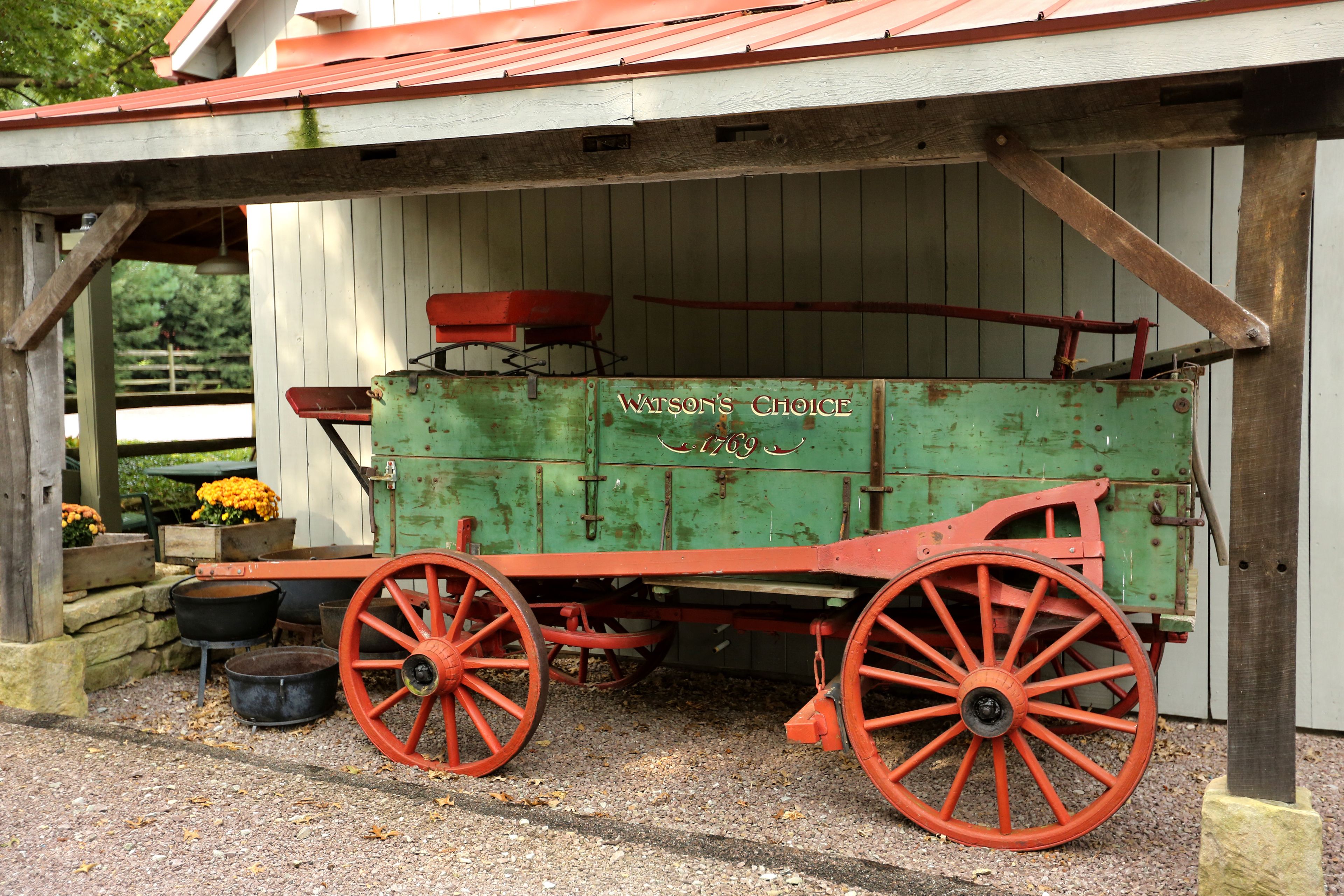 A green and red antique cart labeled "Watson's Choice" with wheels and a wooden structure in the background.
