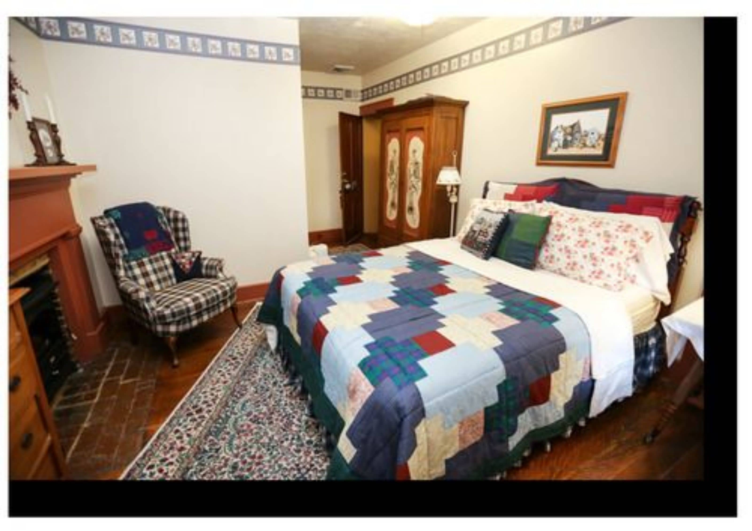 A bedroom with a large bed, a chair, a fireplace, and a rug.