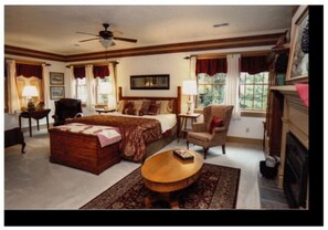 A spacious bedroom with a large bed, a wooden chest, a round coffee table, and a fireplace. - Deer Creek Winery at Watson Estate (Uniontown)