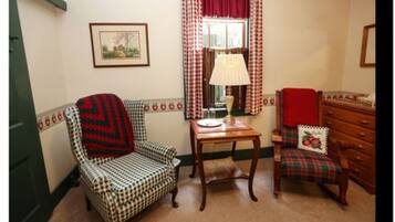 A cozy room with a checkered armchair, a small table with a lamp, a plaid chair, and a wooden dresser.