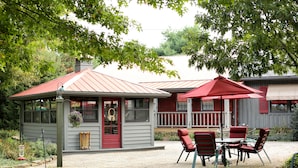 Un patio con mobiliario exterior, un edificio pequeño con puerta roja y un paraguas rojo.