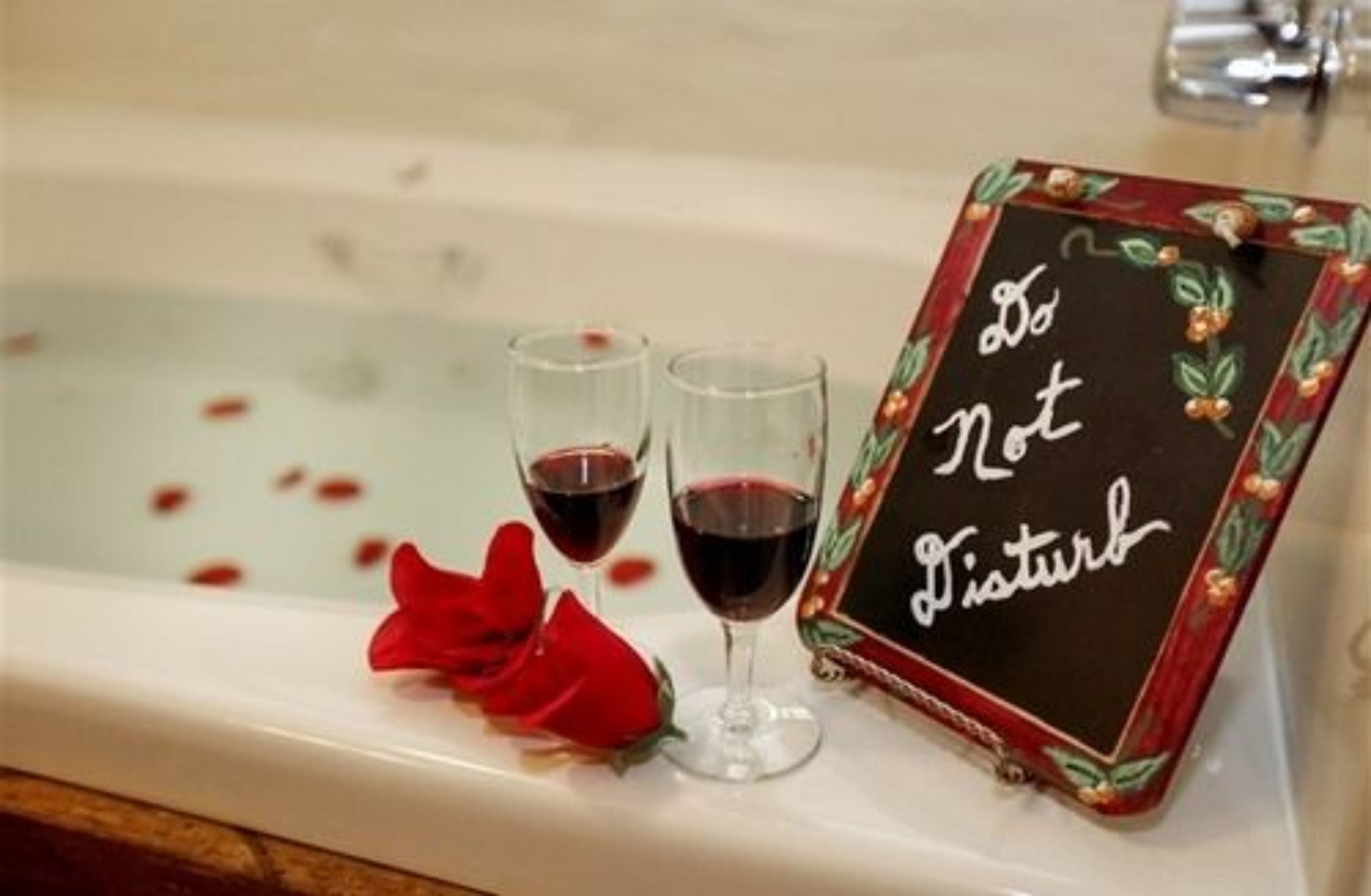 A bathtub with two glasses of red wine and a sign that reads "Do Not Disturb".