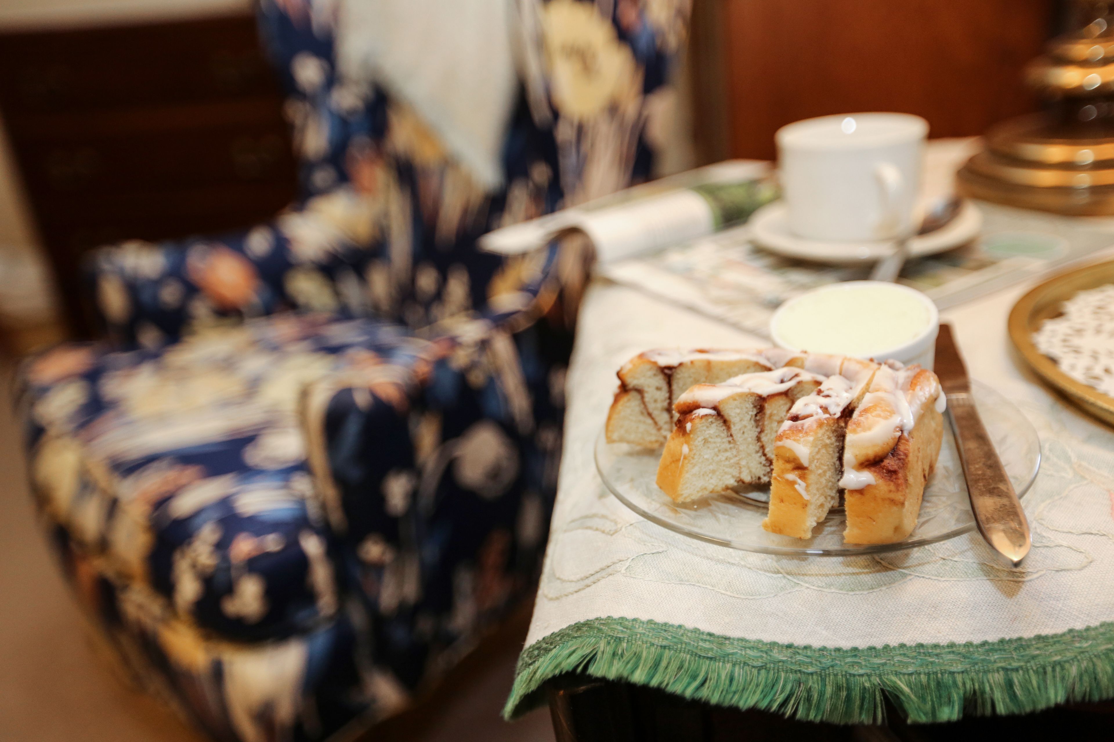 Una mesa con un pastel sobre un plato de vidrio, un cuchillo, una taza y un platito.
