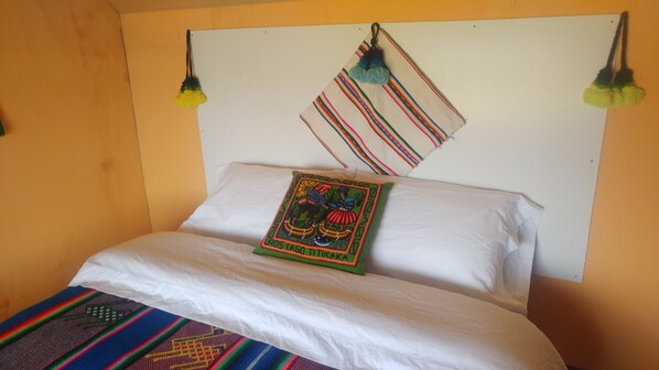 Uma cama com lençóis brancos, um cobertor colorido e um travesseiro decorativo com um desenho tradicional.