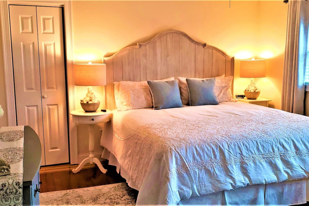 Un dormitorio con una cama grande, dos mesitas de noche con lámparas, un aparador y una puerta.
