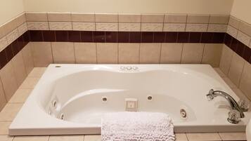 A large, rectangular bathtub with a single faucet and a small control panel, surrounded by beige and dark brown tiles.