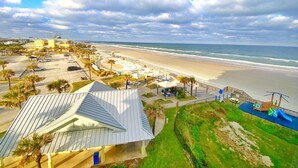 Vista costera con playa, estacionamiento y un edificio con techo inclinado.